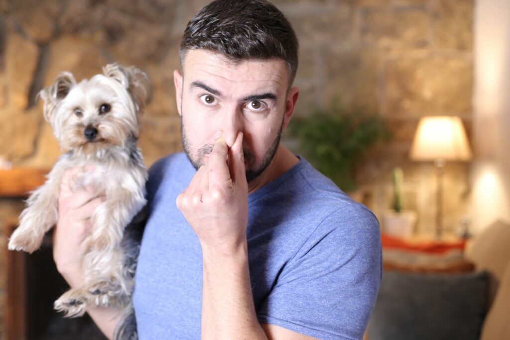 Ein Mann hält einen kleinen Hund auf dem Arm und hält sich die Nase zu.