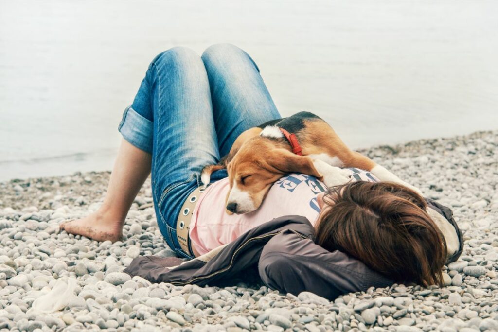 Ein Hund liegt auf dem Bauch seines Frauchen. Entspannung kann gegen den Welpenblues helfen.